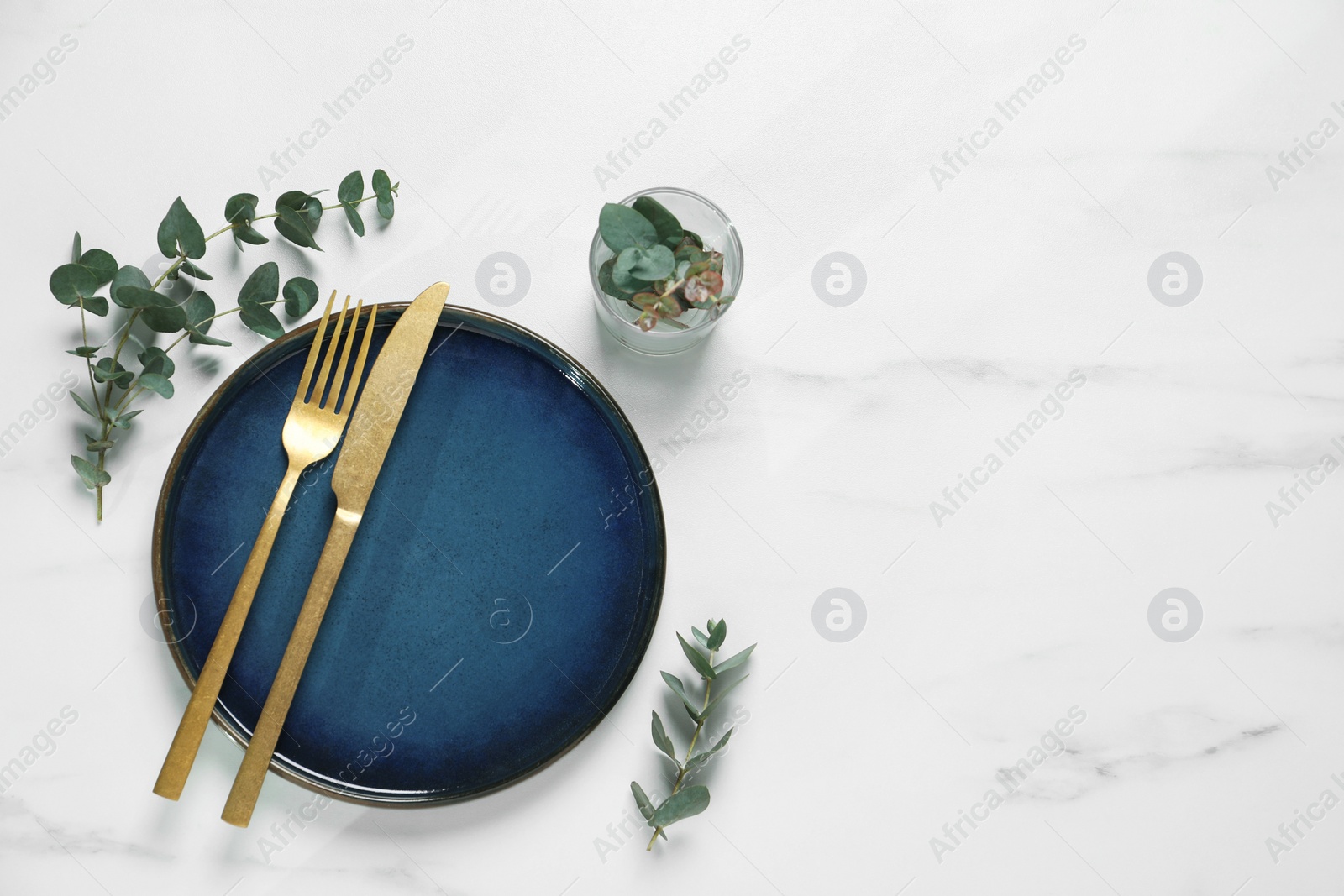 Photo of Stylish setting with cutlery and eucalyptus leaves on white marble table, flat lay. Space for text