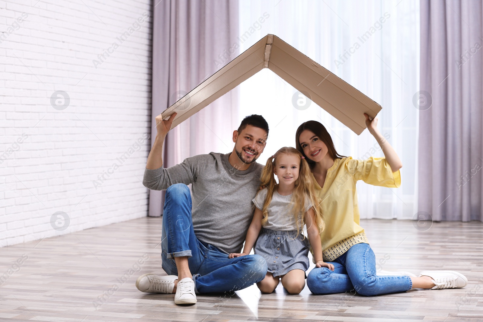 Photo of Happy family sitting under cardboard roof at home. Insurance concept
