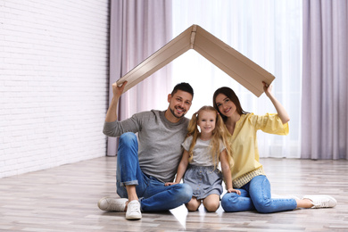 Happy family sitting under cardboard roof at home. Insurance concept