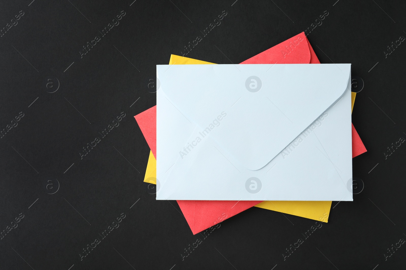 Photo of Stack of colorful paper envelopes on black background, top view