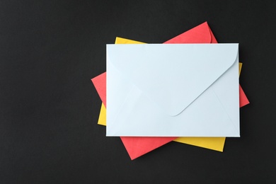 Photo of Stack of colorful paper envelopes on black background, top view