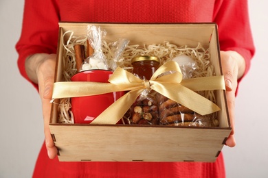 Photo of Woman holding box with stylish craft gift set on light grey background, closeup