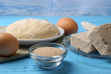 Photo of Different types of yeast, eggs, dough and flour in spoon on light blue wooden table