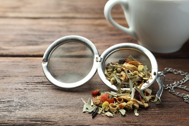 Photo of Snap infuser with dried herbal tea leaves on wooden table, closeup