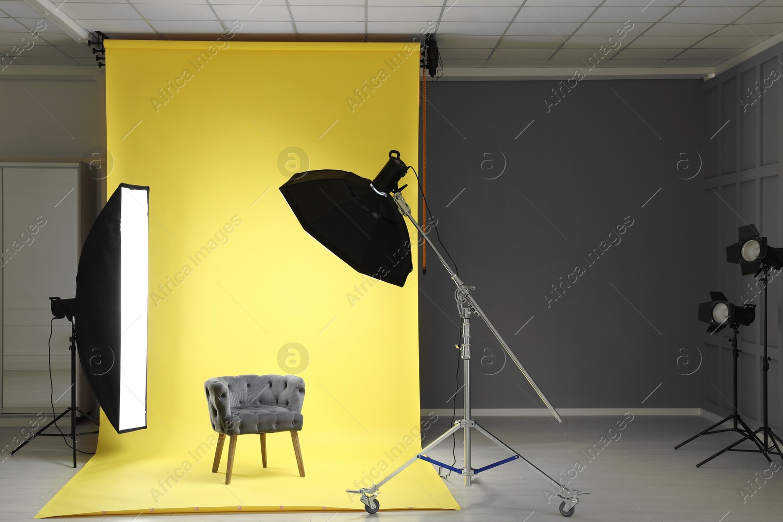 Photo of Yellow photo background, armchair and professional lighting equipment in modern studio