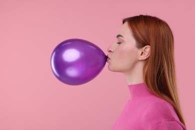 Photo of Woman inflating purple balloon on pink background