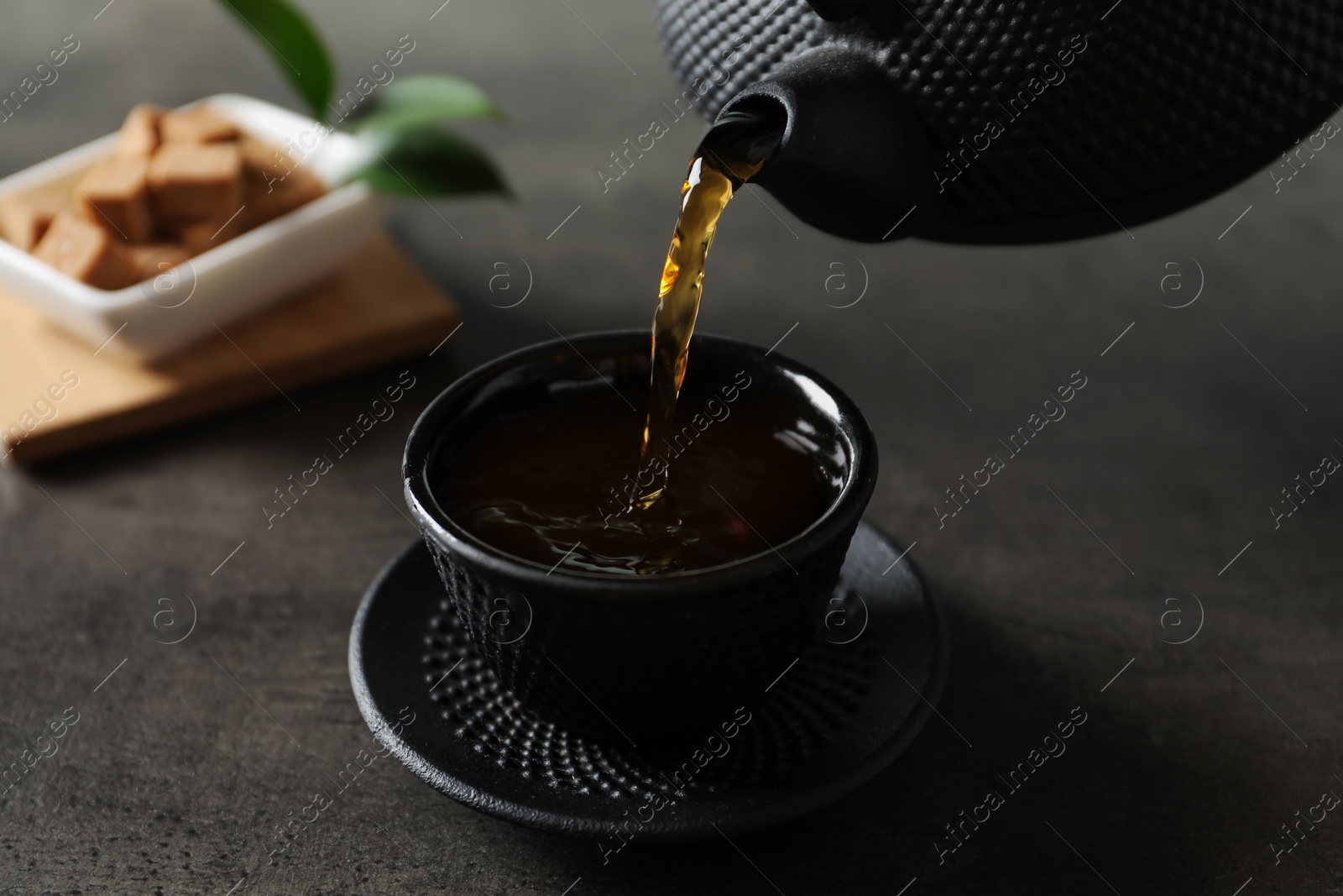 Photo of Pouring hot tea into black cup on dark table