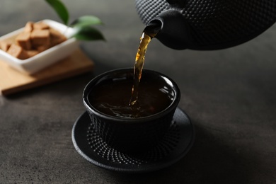 Pouring hot tea into black cup on dark table