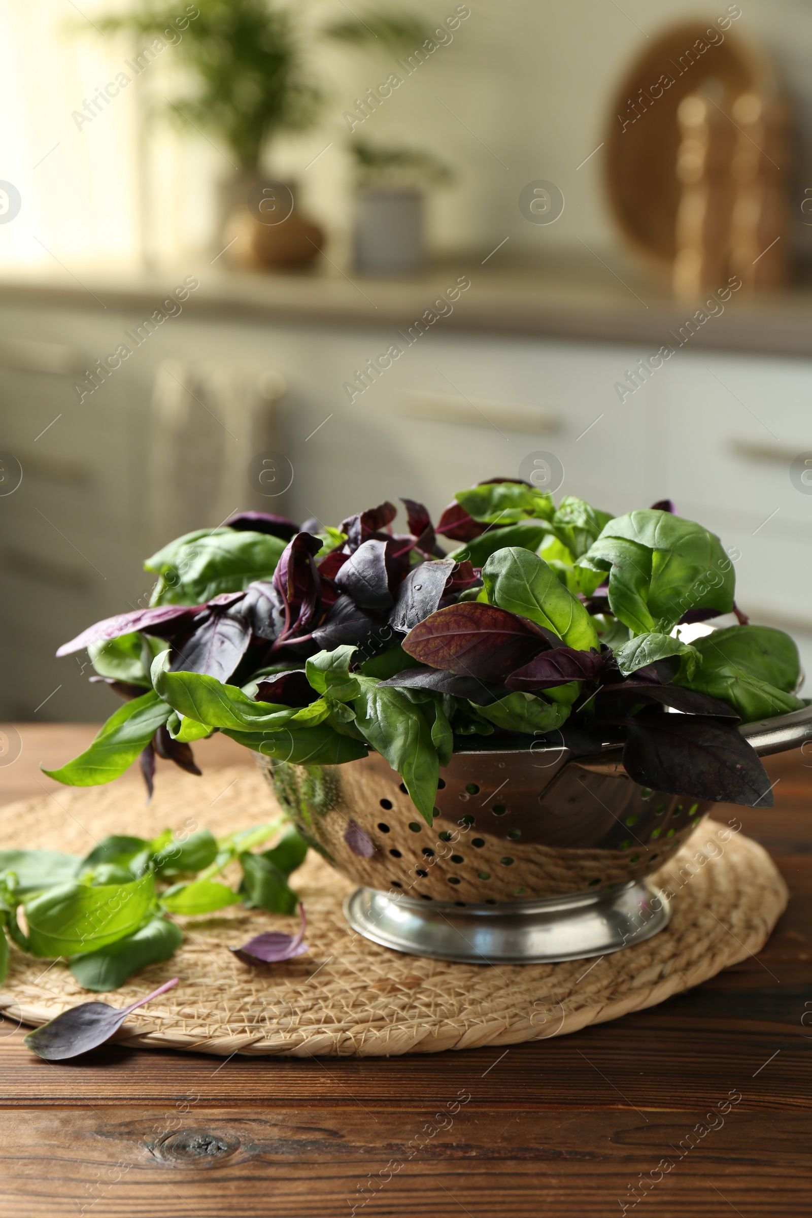 Photo of Metal colander with different fresh basil leaves on wooden table in kitchen