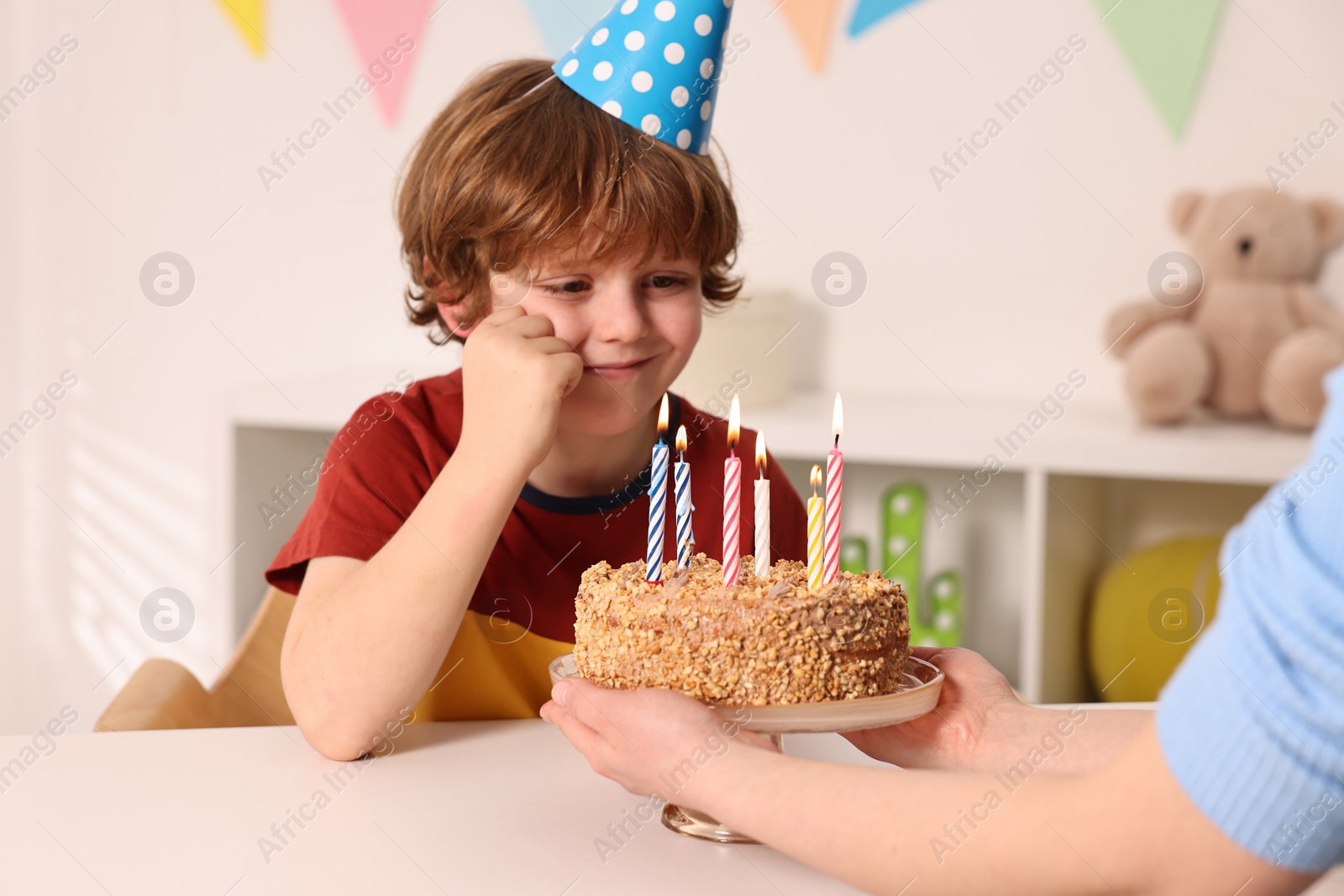 Photo of Birthday celebration. Mother holding tasty cake with burning candles near her son indoors