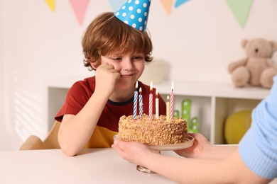 Birthday celebration. Mother holding tasty cake with burning candles near her son indoors