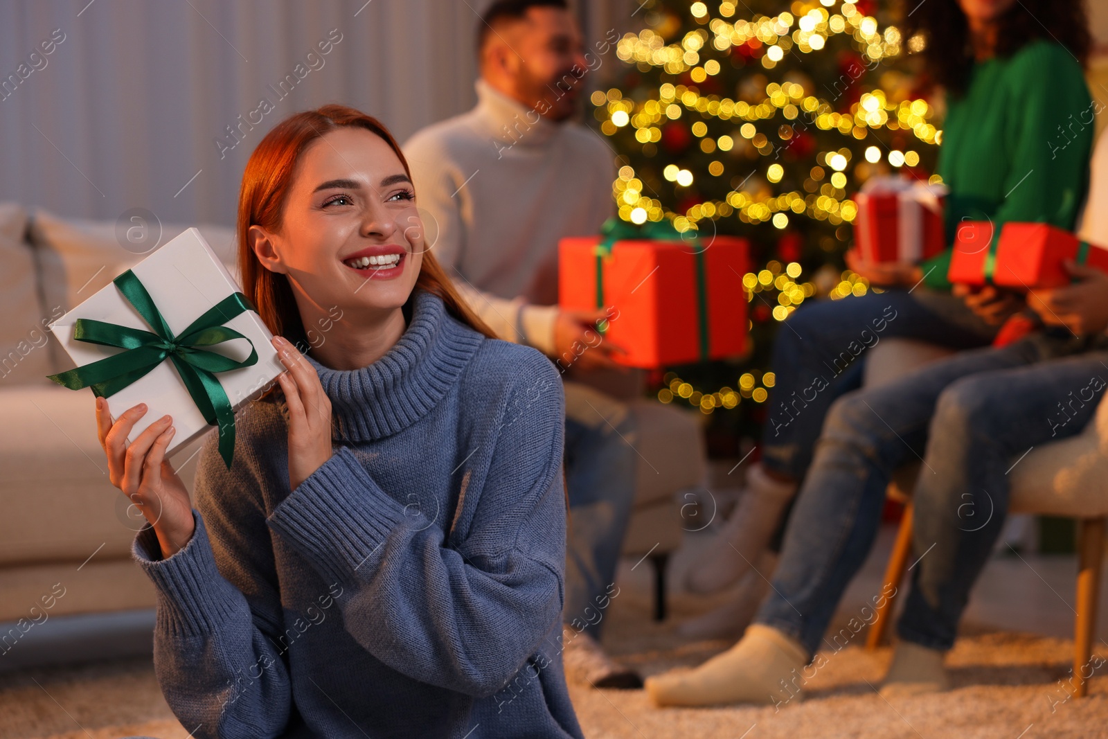 Photo of Christmas celebration in circle of friends. Happy young woman with gift box at home, selective focus