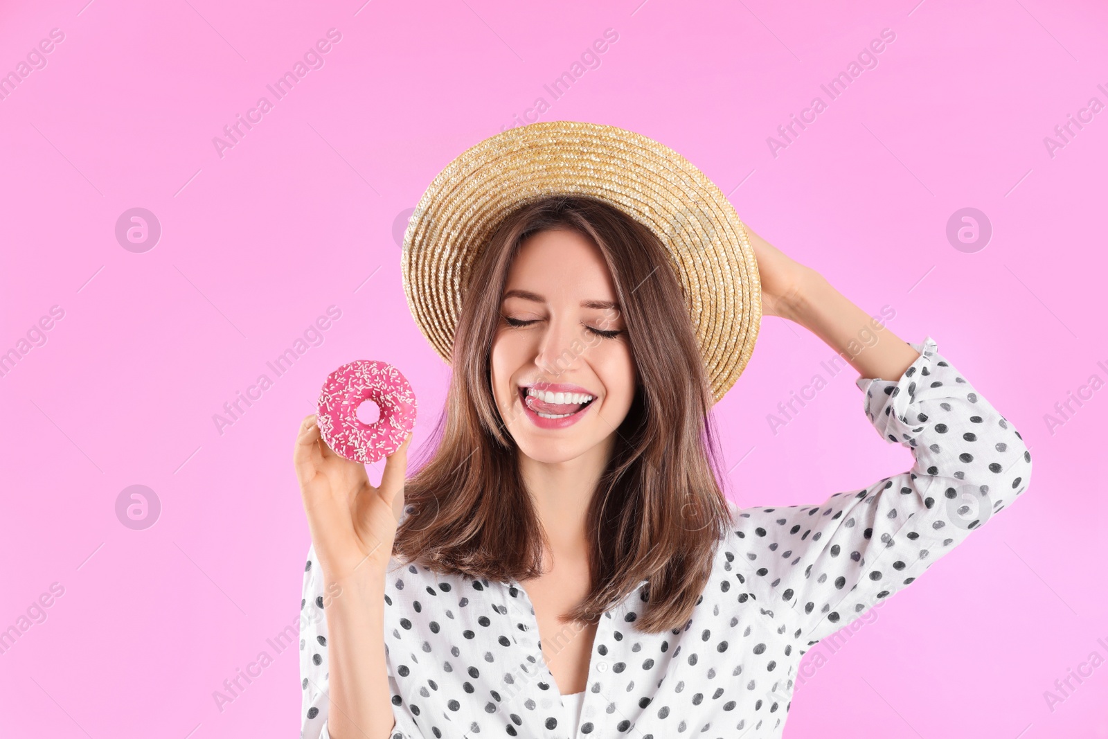 Photo of Beautiful young woman wearing stylish hat with donut on light pink background