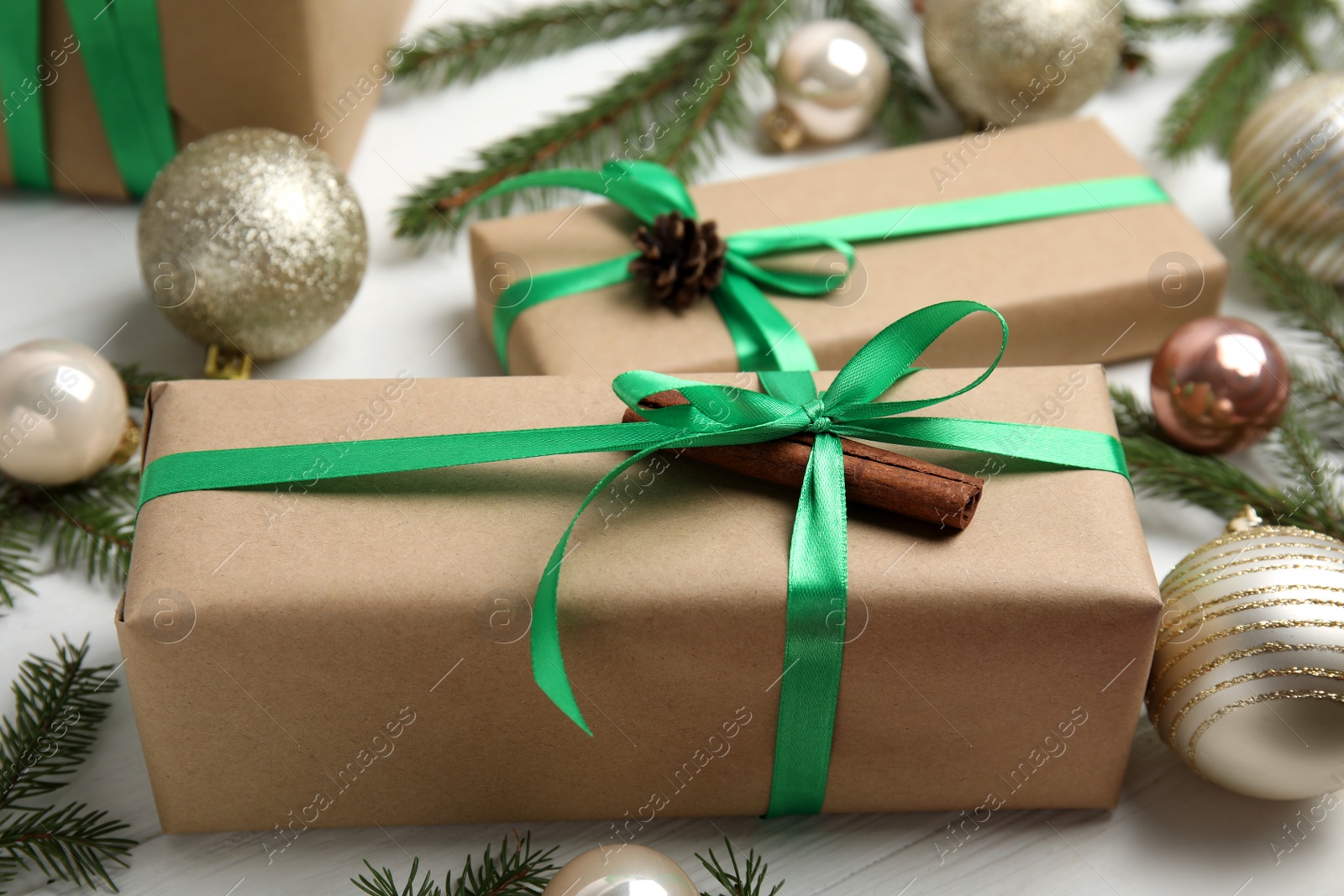 Photo of Gift box with green ribbon and Christmas decor on white wooden table, closeup
