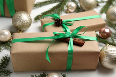 Gift box with green ribbon and Christmas decor on white wooden table, closeup