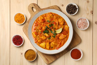 Photo of Delicious chicken curry and spices on wooden table, flat lay