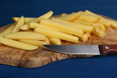 Photo of Cut raw potatoes and knife on blue wooden table, closeup. Cooking delicious French fries