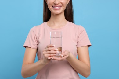 Healthy habit. Happy woman holding glass with fresh water on light blue background, closeup