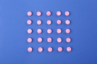 Photo of Many pink vitamin pills on blue background, flat lay