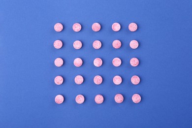 Many pink vitamin pills on blue background, flat lay