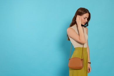 Photo of Beautiful young woman in fashionable outfit with stylish bag on light blue background, space for text