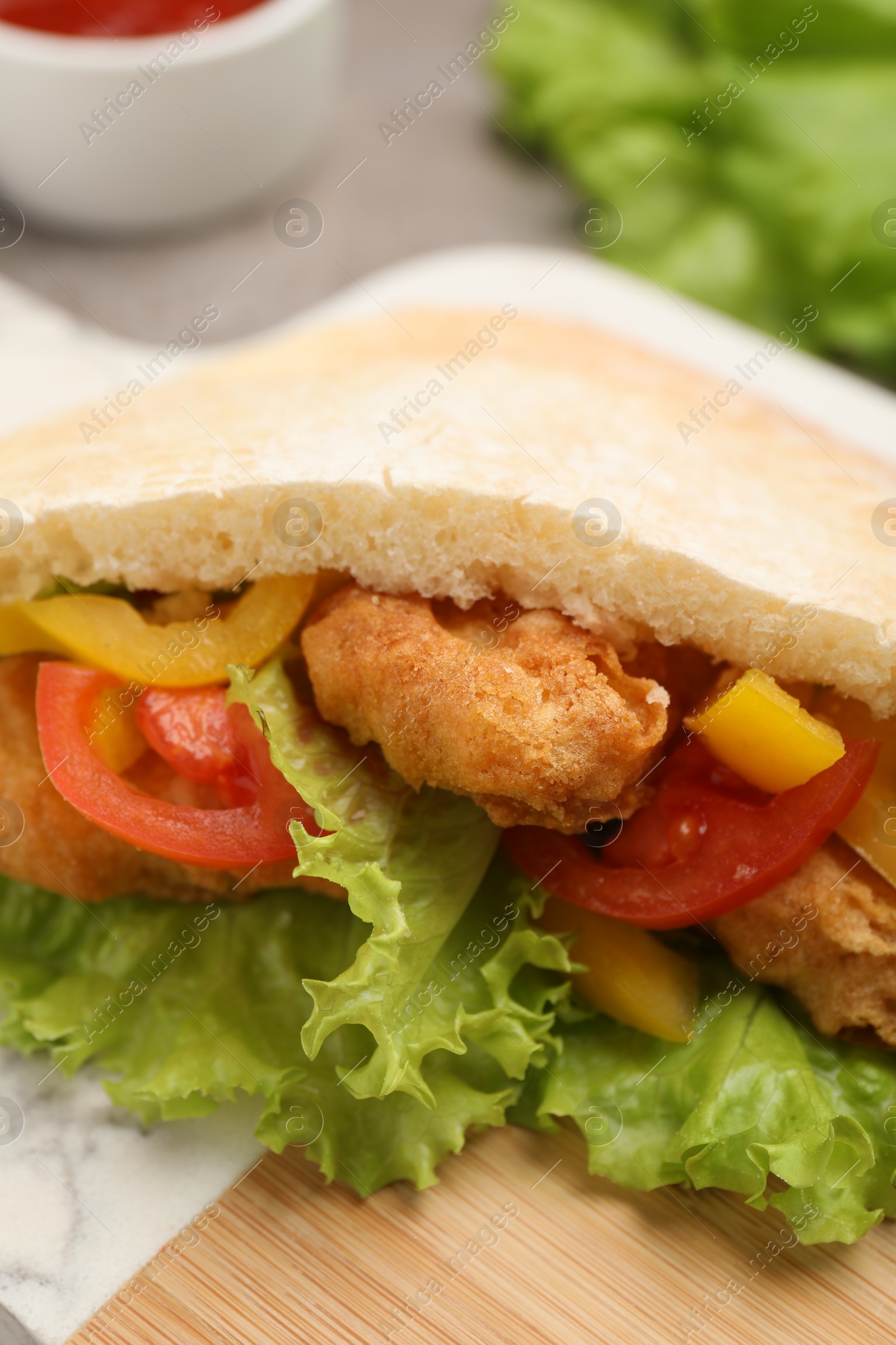 Photo of Delicious pita sandwich with fried fish, pepper, tomatoes and lettuce on table, closeup