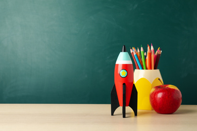 Photo of Bright toy rocket and school supplies on wooden desk. Space for text