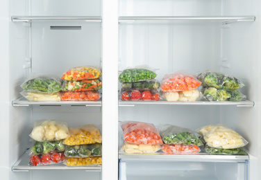 Plastic bags with different frozen vegetables in refrigerator