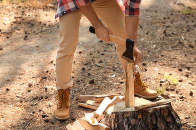 Photo of Man chopping firewood with axe in forest, closeup