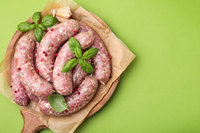 Board with raw homemade sausages, basil leaves and peppercorns on green table, top view. Space for text