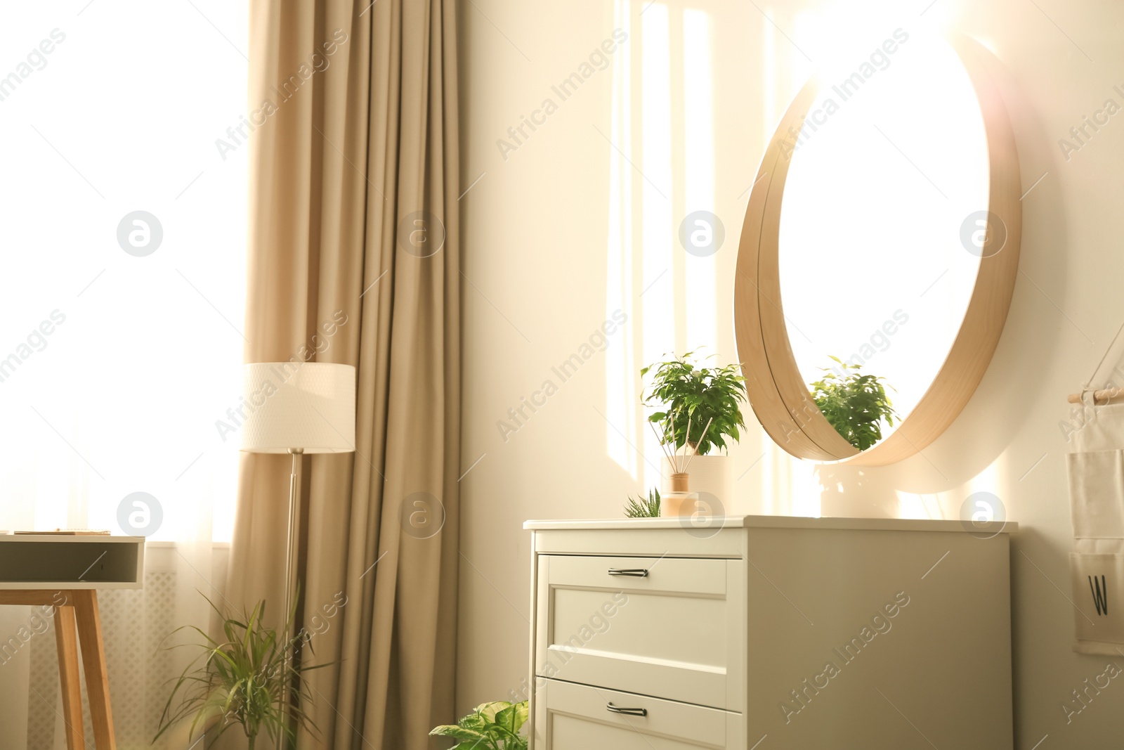 Photo of Stylish room interior with chest of drawers and round mirror