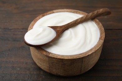 Photo of Delicious natural yogurt in bowl and spoon on wooden table, closeup