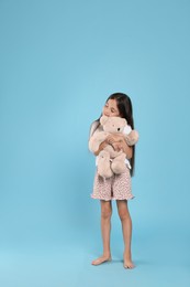 Cute girl wearing pajamas with teddy bear on light blue background