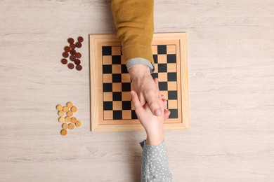 Photo of Playing checkers. Partners shaking hands after match at white wooden table, top view