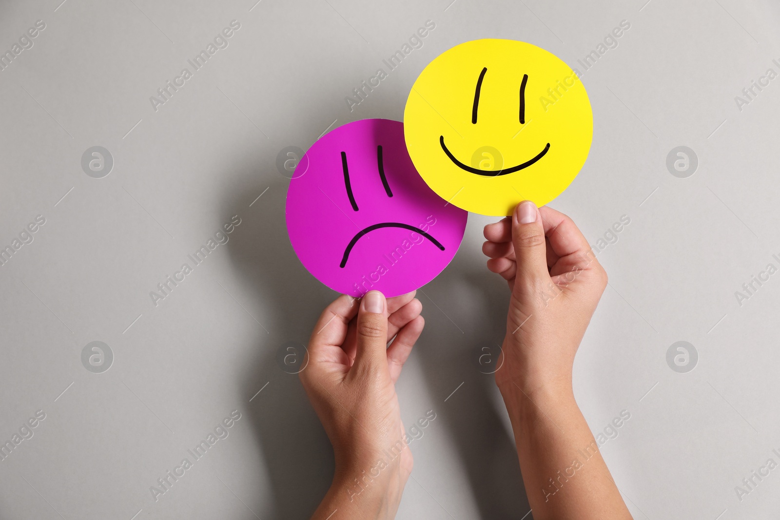 Photo of Choice concept. Woman holding papers with sad and happy emoticons on light grey background, closeup