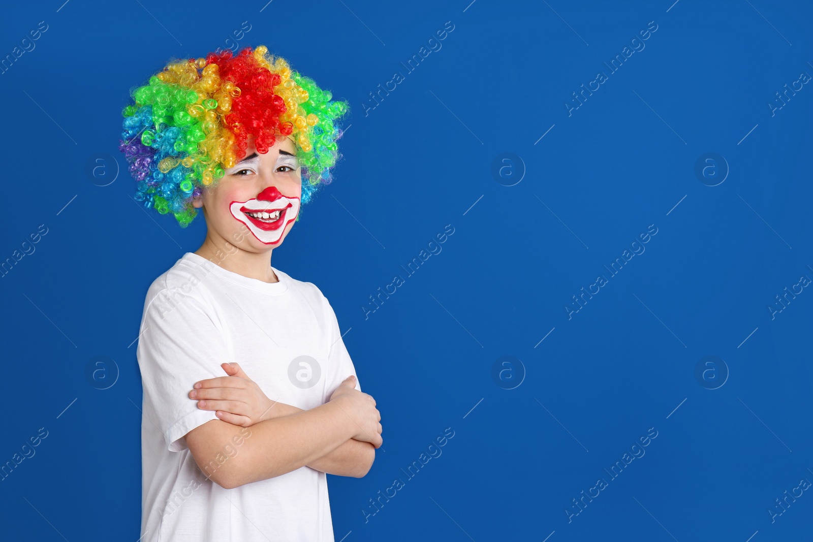 Photo of Preteen boy with clown makeup and wig on blue background, space for text. April fool's day