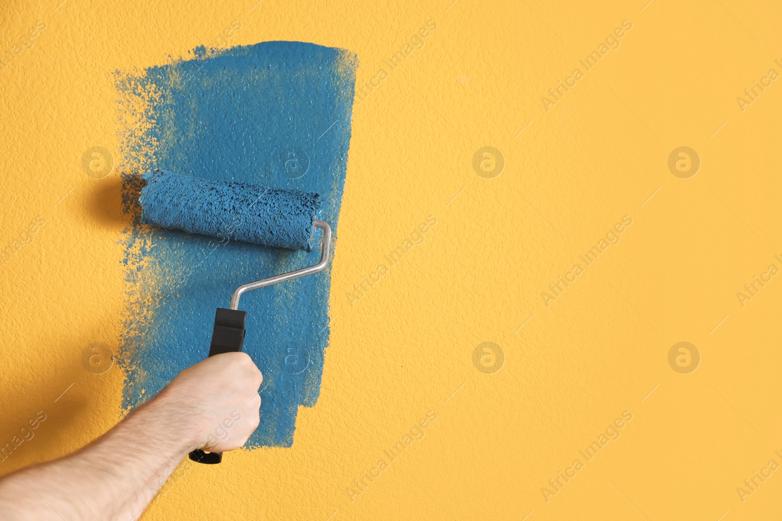 Photo of Man painting yellow wall with blue dye, closeup. Space for text