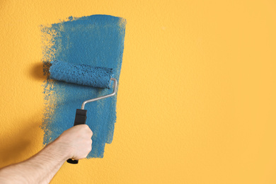 Photo of Man painting yellow wall with blue dye, closeup. Space for text