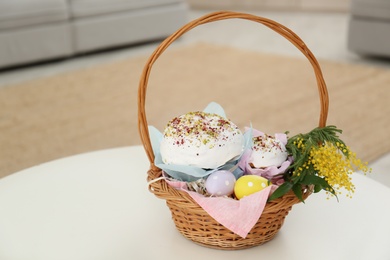 Photo of Basket with delicious Easter cakes, dyed eggs and flowers on white table indoors. Space for text