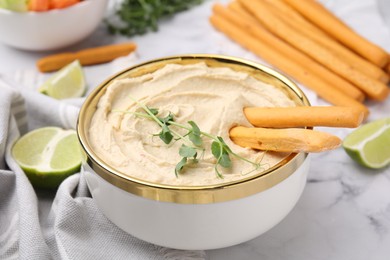 Delicious hummus with grissini sticks served on white marble table, closeup