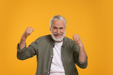 Happy senior sports fan celebrating on yellow background