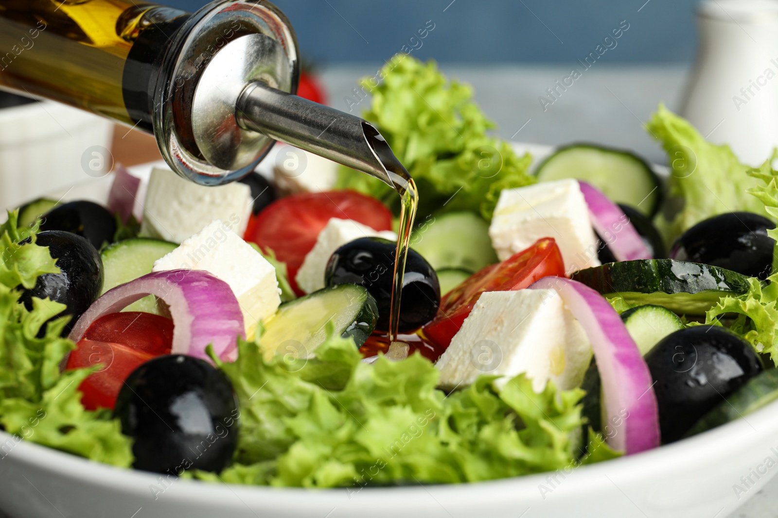 Photo of Dressing tasty fresh Greek salad with olive oil, closeup