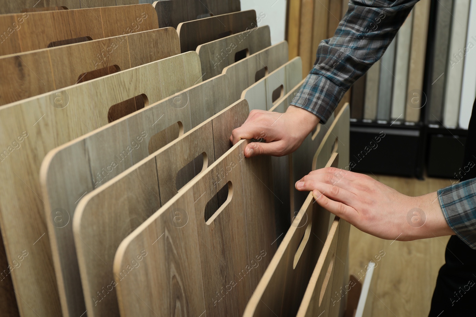 Photo of Man choosing wooden flooring among different samples in shop, closeup