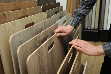 Photo of Man choosing wooden flooring among different samples in shop, closeup