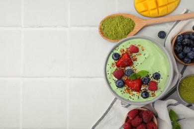 Tasty matcha smoothie bowl served with berries and oatmeal on white tiled table, flat lay with space for text. Healthy breakfast