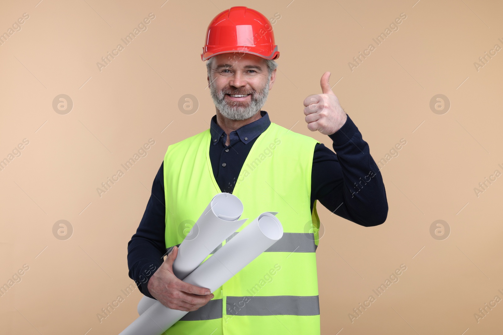 Photo of Architect in hard hat holding drafts and showing thumb up on beige background