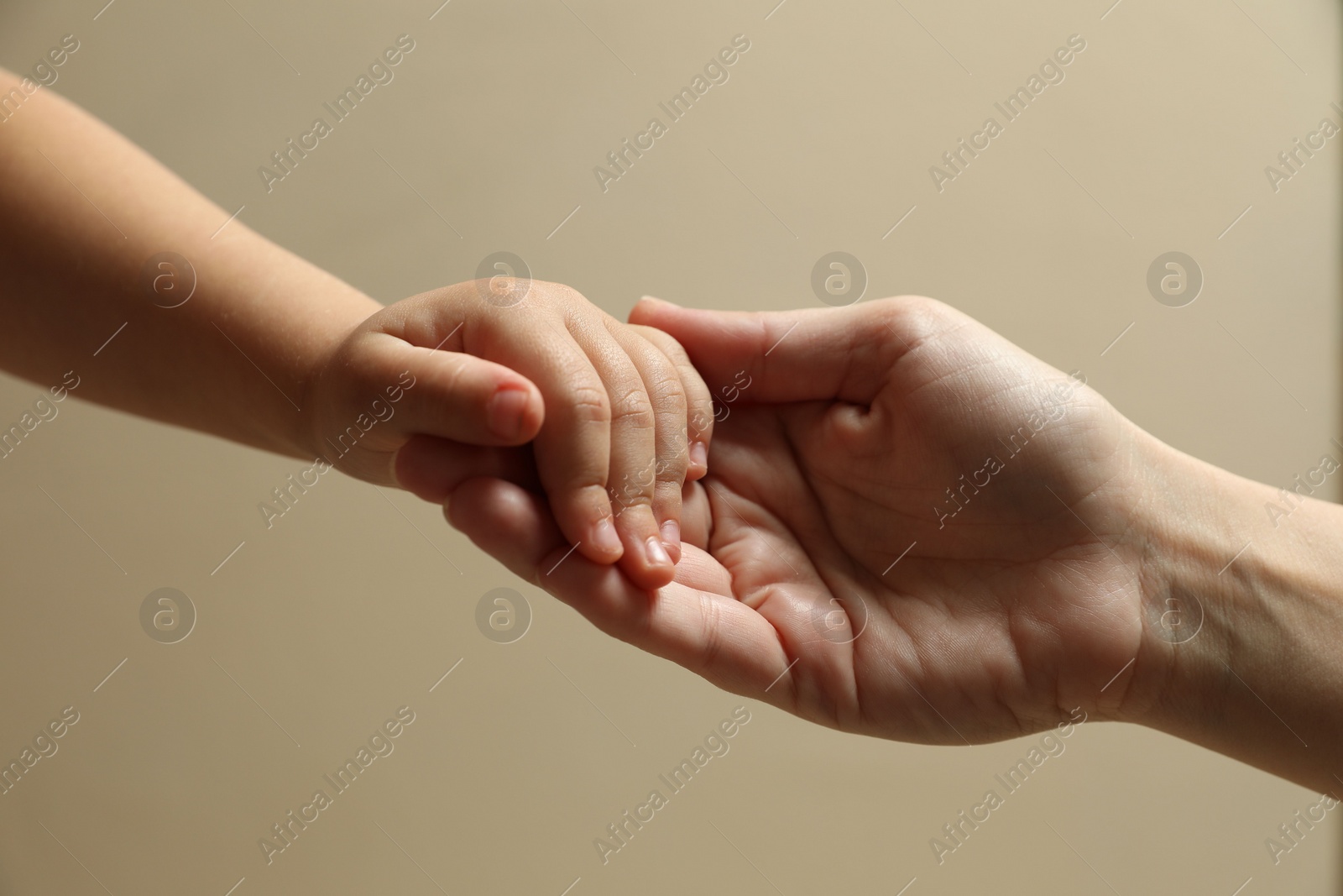 Photo of Mother and child holding hands on beige background, closeup