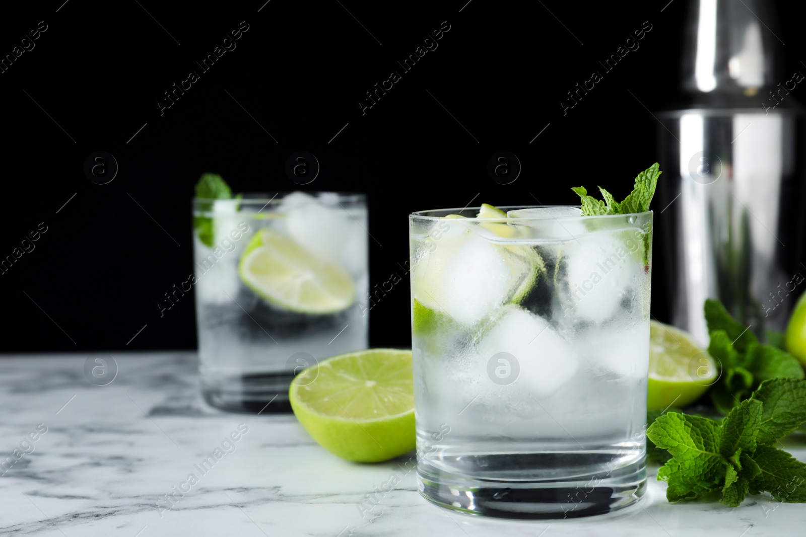 Photo of Glass of cocktail with vodka, ice and lime on white marble table against black background. Space for text