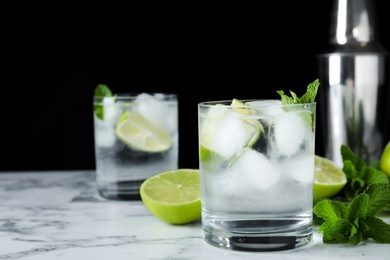 Glass of cocktail with vodka, ice and lime on white marble table against black background. Space for text