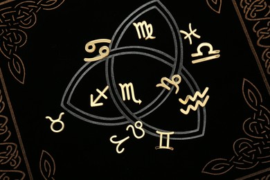 Photo of Zodiac signs on dark book, flat lay